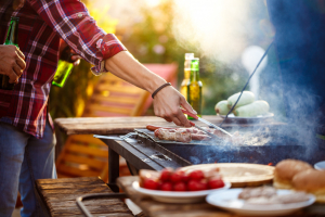 młody mężczyzna przewraca kiełbaski i inne rzeczy na grillu