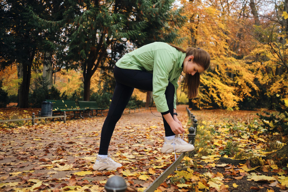 Piękna sportowa dziewczyna wiążąca sznurowadła w trampkach przed biegiem w przytulnym jesiennym parku