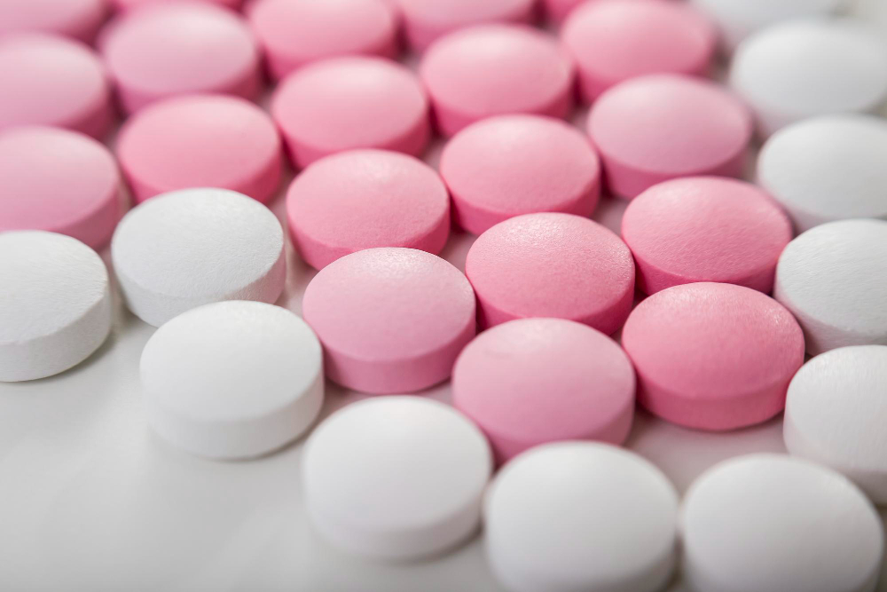 Zbliżenie białych i różowych tabletek leżących na białym biurku.