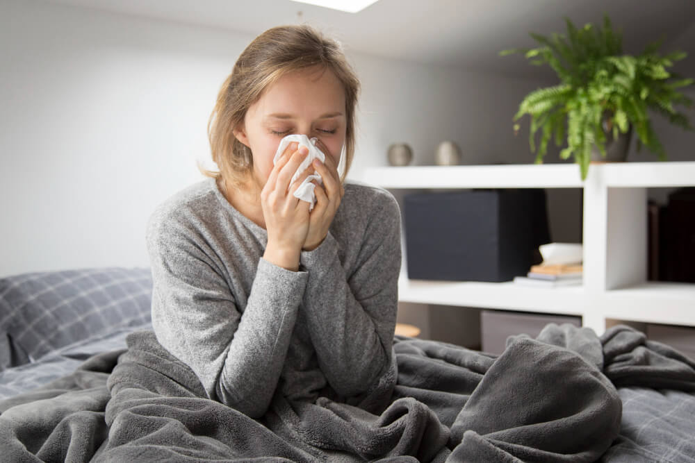 infekcja wirusowa – kobieta siedząca na łóżku, wydmuchująca nos w chusteczkę