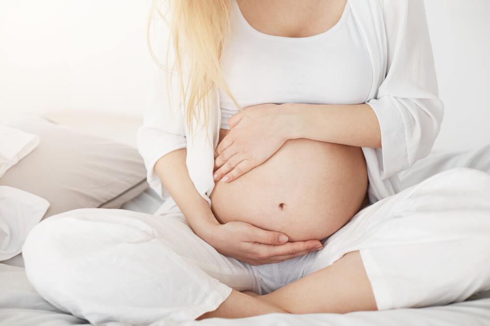kobieta w ciąży otaczająca rękami ciążowy brzuch