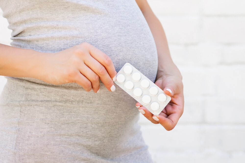 liczne bakterie w moczu w ciąży – kobieta w ciąży trzymająca w dłoniach opakowanie tabletek