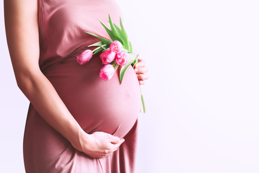 Kobieta w ciąży z kwiatami trzyma ręce na brzuchu na białym tle koncepcja wakacji na dzień matki