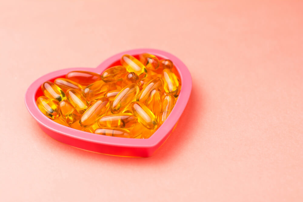 tabletki z tranem w pudełeczku w kształcie serca na różowym tle