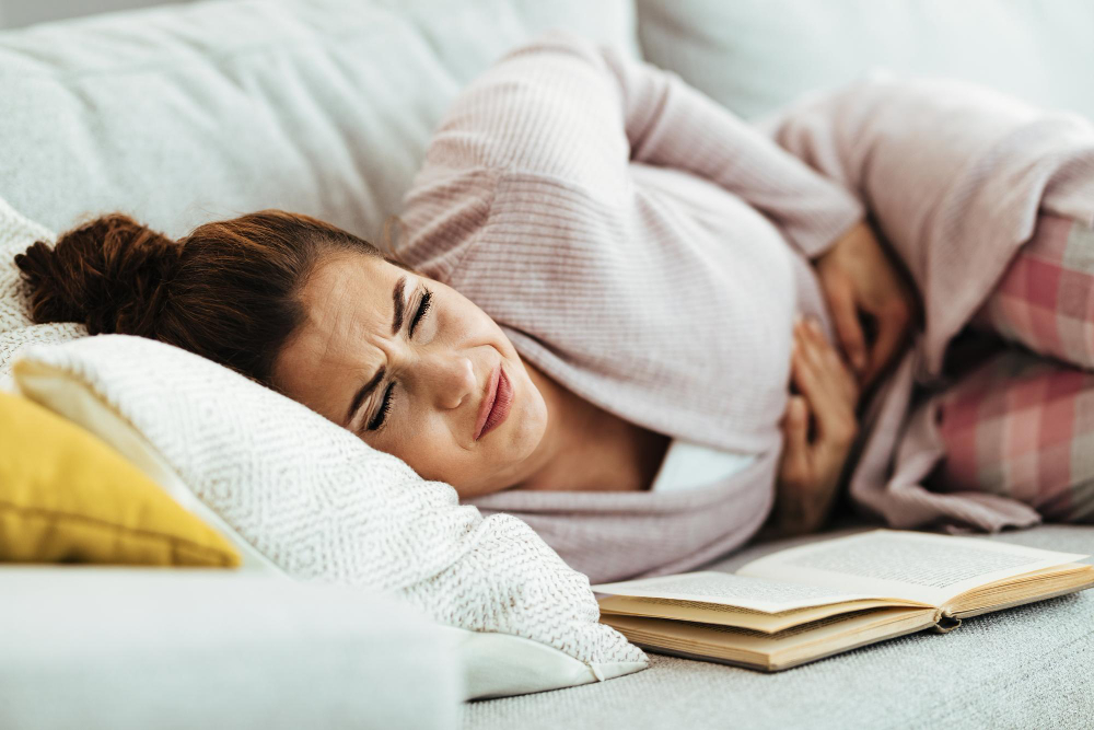 Młoda kobieta odczuwa ból brzucha, leżąc na kanapie w domu