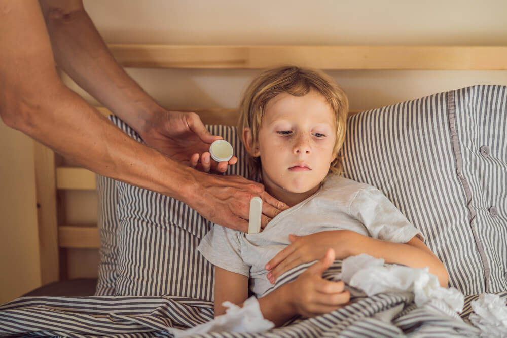 domowy sposób na suchy kaszel – tata aplikujący maść rozgrzewającą choremu synowi