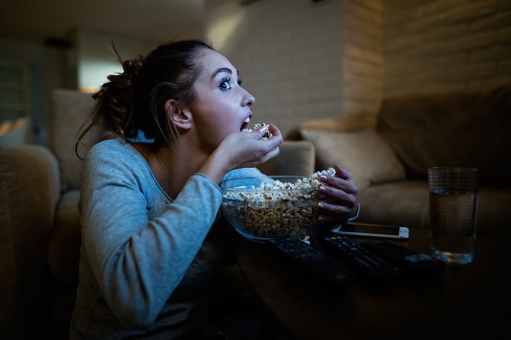 młoda kobieta czuje głód i je popcorn z miski podczas nocnego oglądania filmu w domu